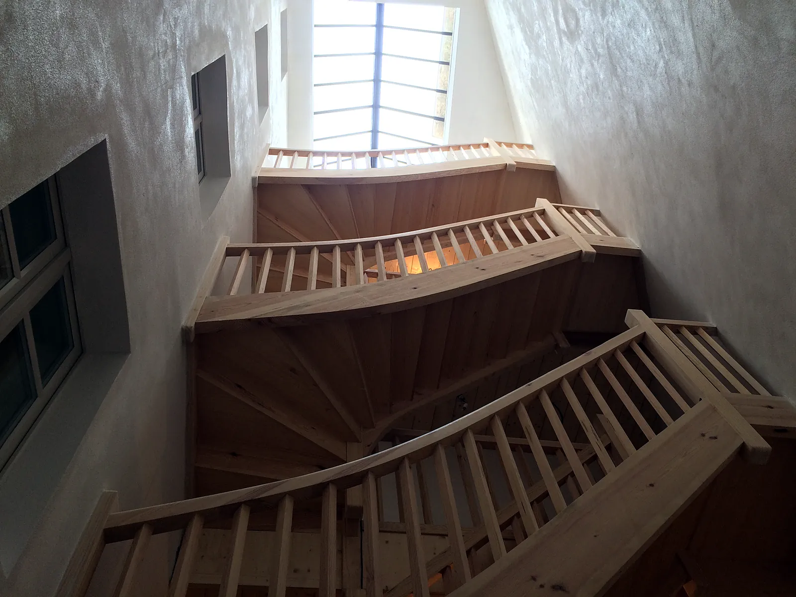 Escalier en bois à marches balancées et garde-corps à barreaux dans une cage d'escalier sous verrière